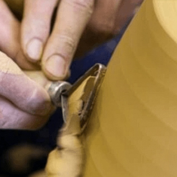 Nahaufnahme von Händen, die mit einem Meißel ein sich drehendes Stück Holz auf einer Drehbank im Aurora Tierkrematorium in Form bringen, wobei die Holzspäne wegrollen. Aurora Tierkrematorium