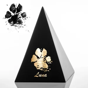Schwarzes pyramidenförmiges Objekt mit einem goldenen Pfotenabdruck und dem eingravierten Namen "Luna"; ein schwarzer Pfotenabdruck ist in der oberen linken Ecke des Bildes sichtbar. Aurora Tierkrematorium