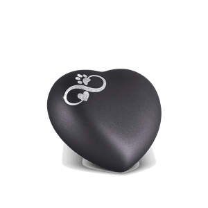 Ein mattschwarzes, herzförmiges Objekt mit einem Design aus zwei ineinander verschlungenen Unendlichkeitssymbolen, einem Pfotenabdruck und einem kleinen Herz auf der Oberfläche. Aurora Tierkrematorium