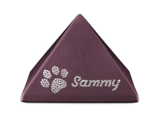 Ein pyramidenförmiges, dunkelviolettes Objekt zeigt auf einer Seite einen strassbesetzten Pfotenabdruck und den Namen "Sammy" in Strasssteinen. Aurora Tierkrematorium